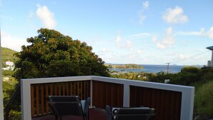 A balcony with two chairs, a wooden railing, and a view of the ocean and hills.