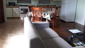 A compact kitchen with a dining table, chairs, a sofa, and a refrigerator.