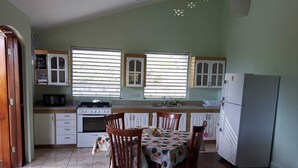A kitchen with a dining table, chairs, a stove, cabinets, and a refrigerator.