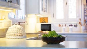 A kitchen with a bowl of green grapes on the counter, a white basket, and a microwave in the background. - Boutique Villa Andronice with amazing view at the Ionian Sea (Tsoukalades)