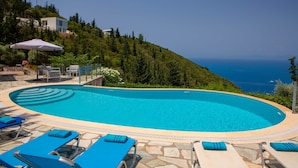 A swimming pool with lounge chairs and an umbrella, surrounded by greenery and a view of the sea. - Boutique Villa Andronice with amazing view at the Ionian Sea (Tsoukalades)