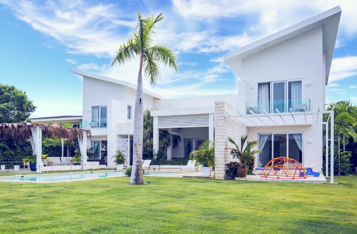Une maison moderne à deux étages, dotée d’une grande pelouse à l’avant, d’une piscine et d’un espace extérieur aménagé avec des sièges.