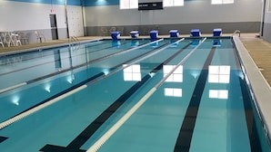 Uma grande piscina interior com várias pistas de natação, iluminação suspensa e janelas.