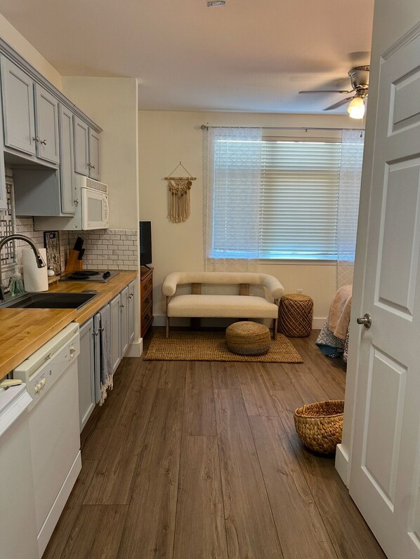 A compact kitchen with wooden countertops, a microwave, and a sink. There is a beige sofa and a small rug in the living area. - Lovely studio at Mariners Landing!  (Huddleston)