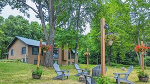 A house with a sloped roof and a well-maintained lawn. There are three Adirondack chairs arranged around a small table. - Secluded 3BR, 2BA ,¼ Mile Off Road , Starry Skies & Wildlife Views (Mosinee)