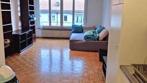 Una stanza con un letto, una finestra, un termosifone e angolo cottura.
