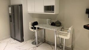 Kompakti keittiö, jossa on jääkaappi, mikroaaltouuni, pieni pöytä ja kaksi baarituolia.