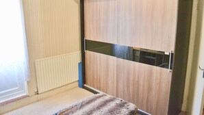 Makuuhuoneessa on liukuovellinen puinen vaatekaappi, patteri ja ikkuna, jossa on verho.