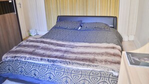 Siististi pedattu sänky, jossa on kuviollinen vuodevaatteisto, puinen pääty ja yöpöytä, jonka päällä on kirja.