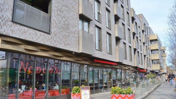 Moderni rakennus, jossa on suuret ikkunat ja näkyvällä paikalla sijaitseva ravintola nimeltä ’Nando’s’.