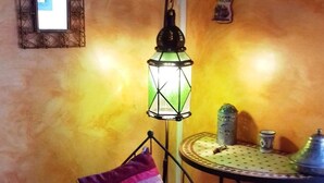 A cozy room with a patterned rug, a chair with a cushion, a table with a decorative item, and a wall-mounted lantern. - Chambre mauresque la maison de josepha (Ferrals-les-Corbières)