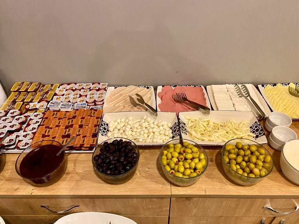 Una mesa de bufé con diversos alimentos, incluyendo tartas, pasta, aceitunas y recipientes con salsas.