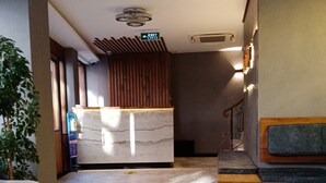 Zona de recepció amb sòl de marbre, taulell de recepció, una banca, una escala i una planta en test.
