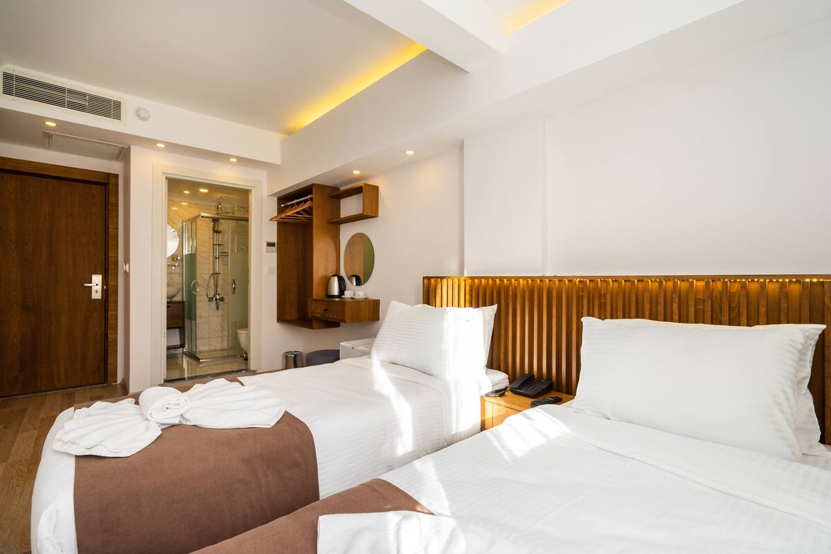 A hotel room with two beds, a wooden headboard, a mirror, and a bathroom visible through an open door.