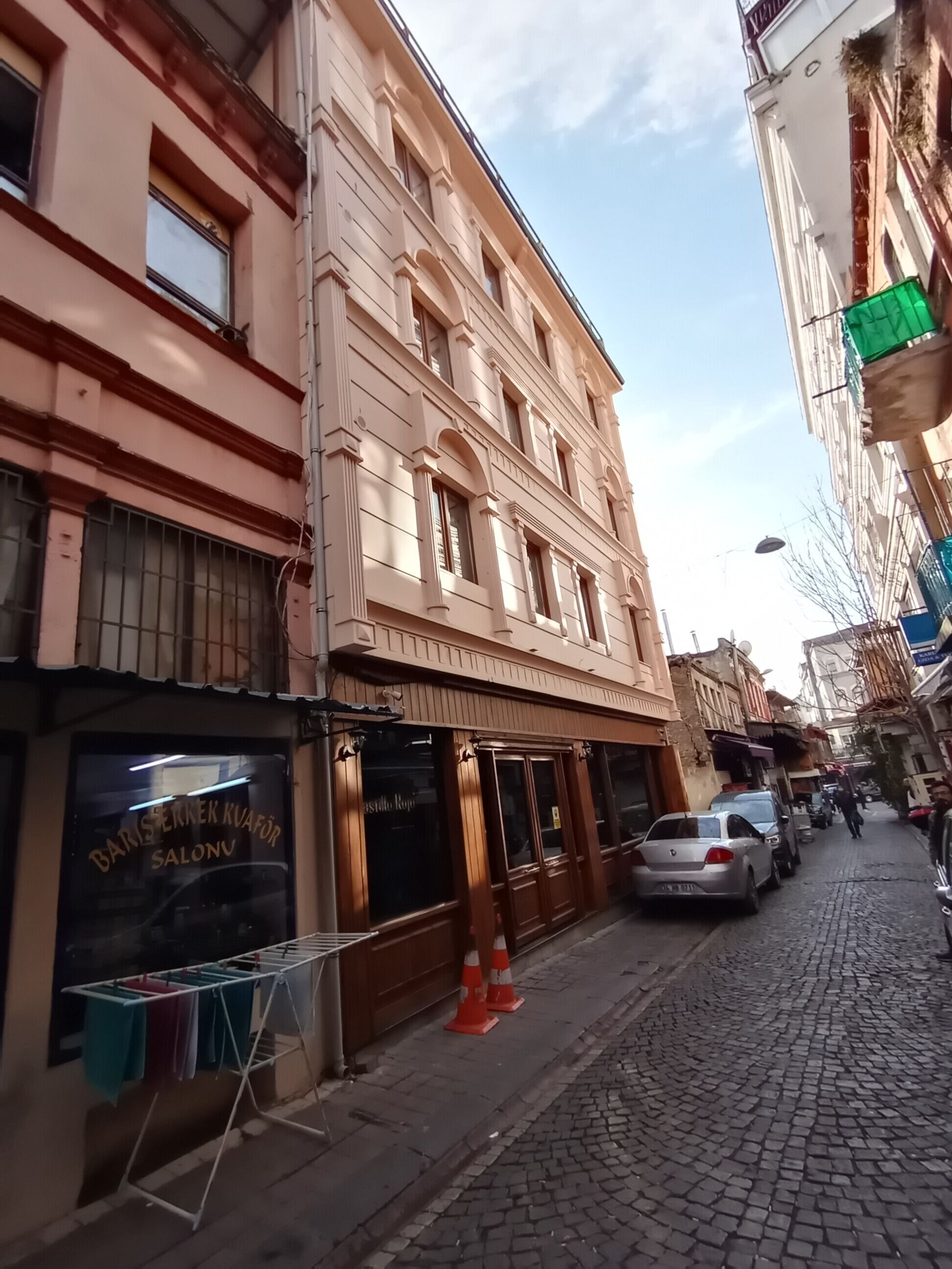 Une rue bordée d’immeubles, avec un salon de coiffure et des voitures garées.