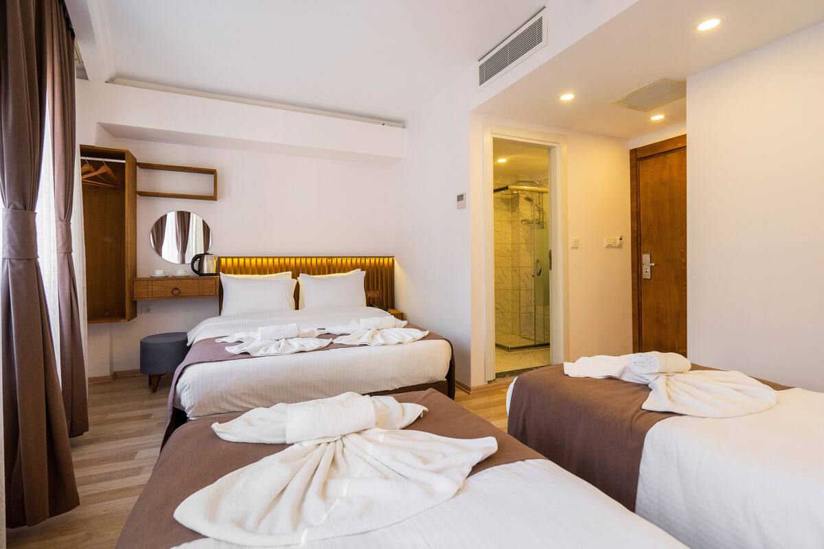 A hotel room with two beds, a walk-in closet, a round mirror, and a shower area.