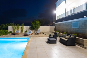 Et poolområde med liggestole, en sofa og en godt oplyst terrasse.