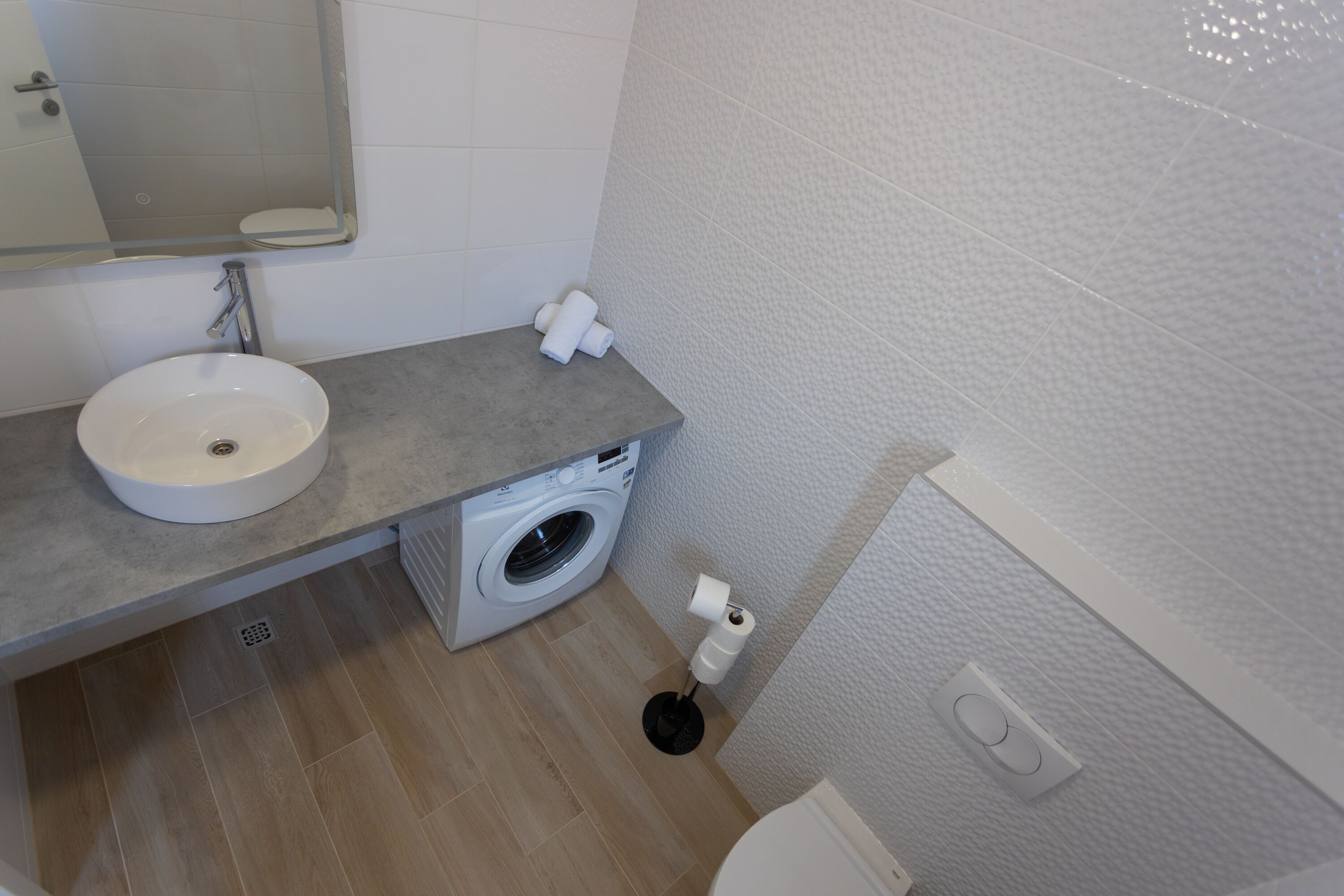 A bathroom with a sink, a washing machine, a toilet, and a mirror.
