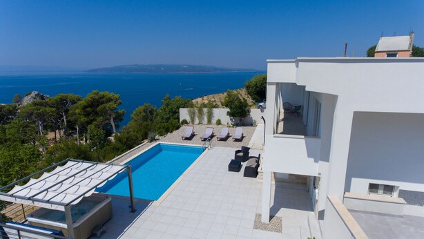A modern building with a swimming pool, outdoor seating, and a view of the sea. - Villa Marko (Makarska)