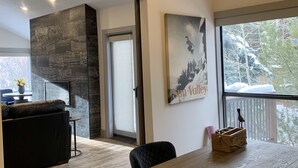 Ein modernes Wohnzimmer mit Kamin, einem Essbereich mit Holztisch und einem großen Fenster mit Blick auf Bäume.