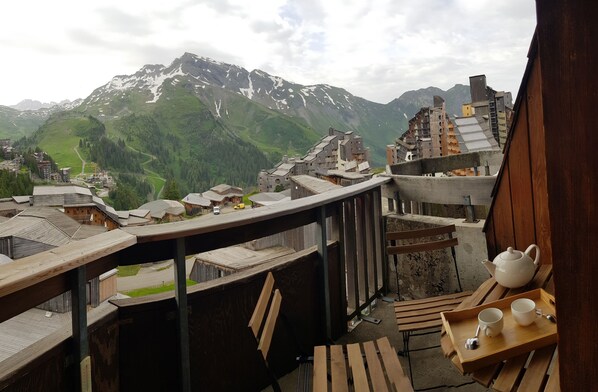 A wooden deck with a table set for tea, overlooking a mountainous landscape with traditional buildings.