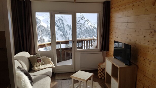 A cozy living room with a sofa, a small table, a TV, and a view of snowy mountains through large windows. - Studio 4 P amazing vue (Avoriaz)