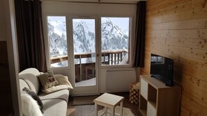 A cozy living room with a sofa, a small table, a TV, and a view of snowy mountains through large windows. - Studio 4 P amazing vue (Avoriaz)