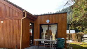 A wooden cabin with a small patio, a table, and a chair. - Chalet Capucine 1 in the heart of the Vosges mountains (Gérardmer)