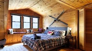 Une chambre dans une cabane en bois, avec un lit, des fenêtres, un plafond en bois et un porte-skis fixé au mur.