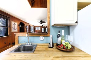Una cocina con encimera de madera, pileta de acero inoxidable, ventilador de techo y un bol de fruta.