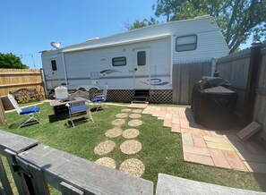 Un véhicule récréatif doté d’un espace extérieur aménagé avec une terrasse en bois, du mobilier de jardin et un barbecue.
