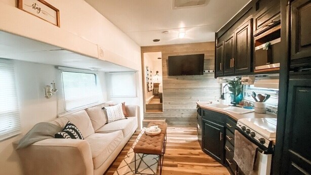 A compact living space with a sofa, ottoman, and a kitchen area including a stove and cabinets. - RV There Yet? Lake view at PK.  (Graford)