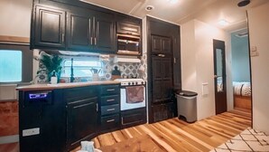 A compact kitchen with dark cabinets, a microwave, and a stove. There's a trash bin and a small table with a tray. - RV There Yet? Lake view at PK.  (Graford)