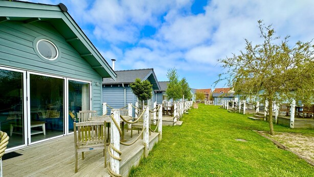 A residential area with a wooden deck, a grassy lawn, and a row of houses with white railings. - Stunning Coastal Beach House - Sleeping 5 in 2 Bedrooms - Pool and Beach Access Included. (Filey)