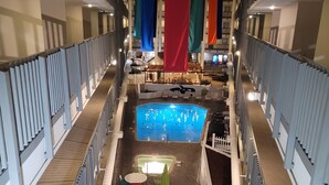 Ein Poolbereich mit einem zentralen Pool, Liegestühlen und Tischen. Bunte Flaggen hängen von der Decke.