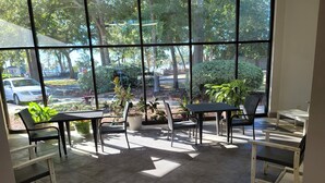Eine sonnendurchflutete Terrassenfläche mit Tisch und Stühlen, große Fenster mit Blick auf die Straße und die umliegende Natur.