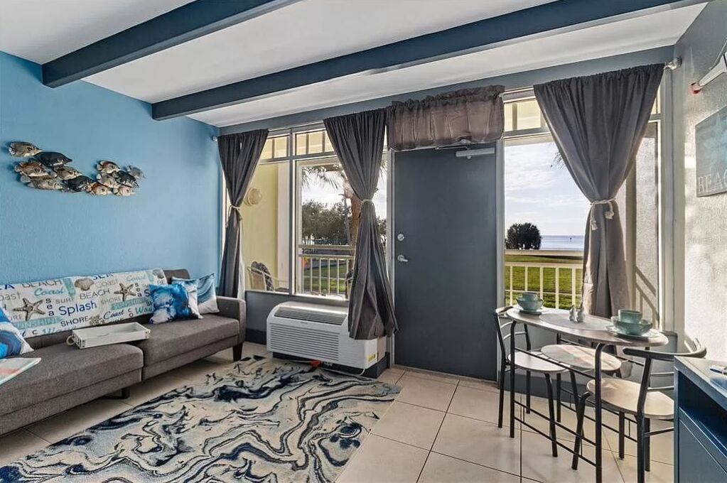 Un salon comprenant un canapé, une table à manger avec des chaises, une grande fenêtre avec des rideaux et un mur décoré avec un motif de poissons.