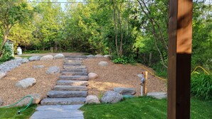 A stone pathway leading through a landscaped garden with a wooden post and a hose on the right. - Fully renovated luxury waterfront cottage (Havelock)