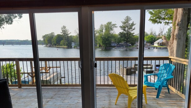 A room with a view of a lake, a deck with chairs, and a wooden floor. - Fully renovated luxury waterfront cottage (Havelock)