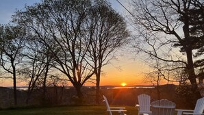 Une vue sur le coucher de soleil avec trois chaises Adirondack disposées dans un espace herbeux.