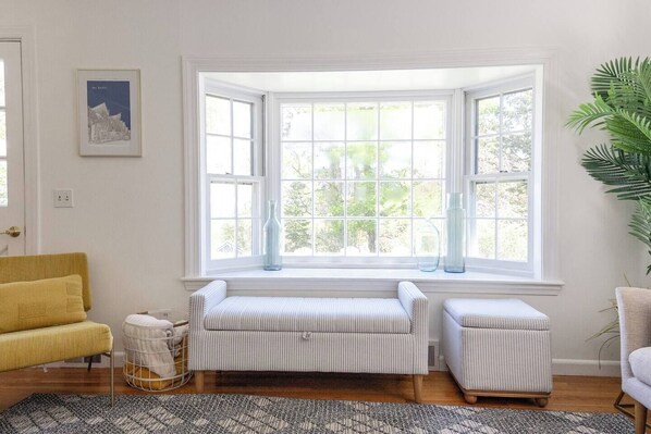 A room with a bay window, a yellow armchair, a striped bench, and a potted plant.