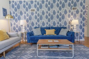 A living room with a blue sofa, a grey couch, a wooden coffee table, and patterned wallpaper.