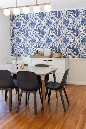 A dining area with a wooden table, four chairs, a white cabinet, and a blue floral wallpaper.