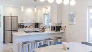Une cuisine moderne avec des meubles blancs, un réfrigérateur en acier inoxydable, un îlot central doté de tabourets et un éclairage suspendu.