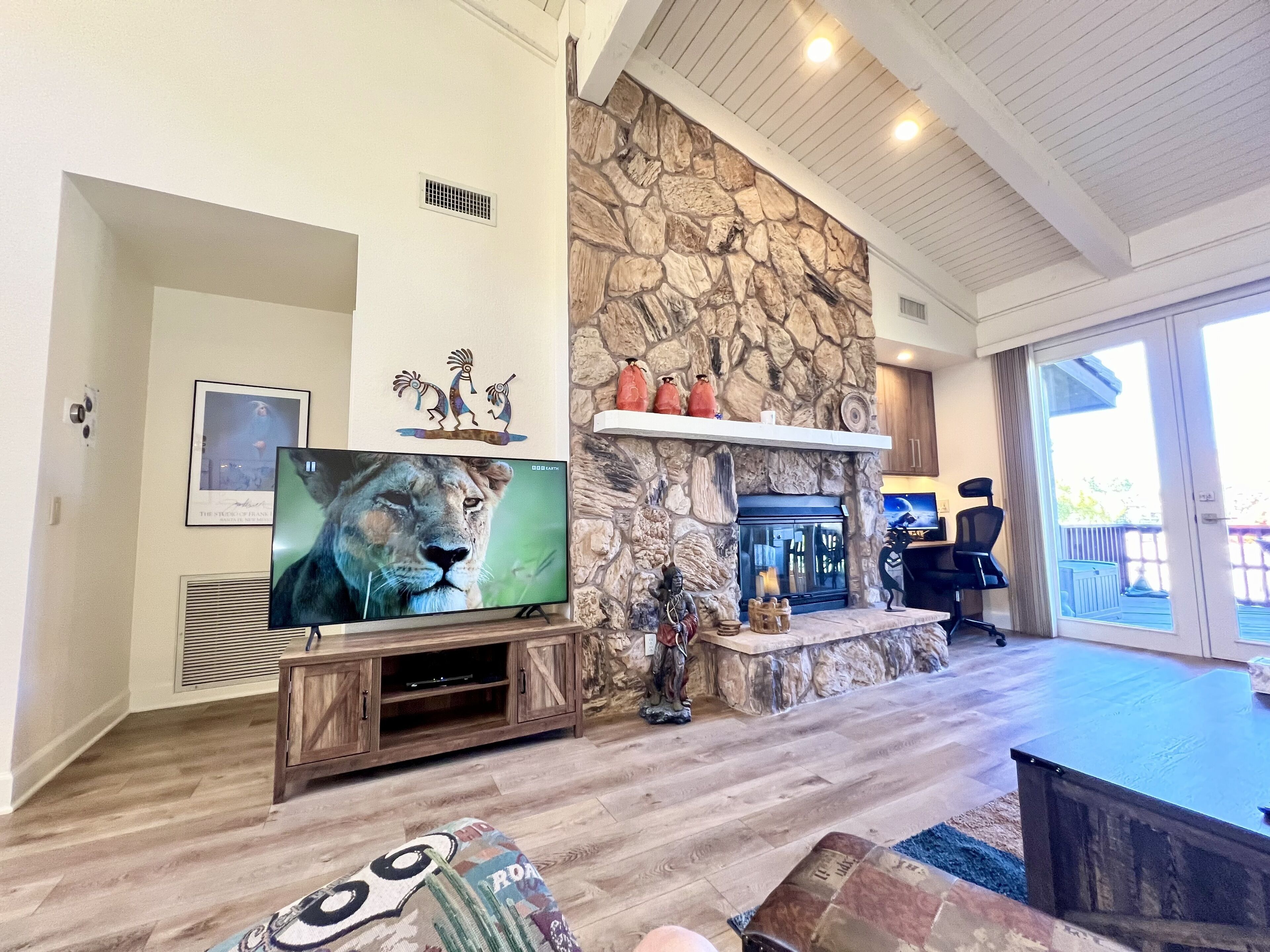 A living room with a stone fireplace, a mounted television, and a wooden entertainment unit.