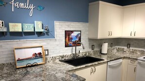 A kitchen with white cabinets, a granite countertop, a sink, and a stove. There are decorative items on the wall and a framed picture on the counter. - Vanderbilt Beach less than a mile! Dog friendly, Tropical Paradise! 3br & WiFi! (Naples)