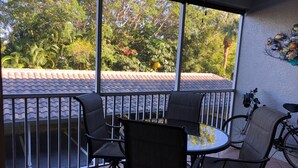 A covered outdoor seating area with a table and chairs, a bicycle, and a view of a tiled roof and greenery. - Vanderbilt Beach less than a mile! Dog friendly, Tropical Paradise! 3br & WiFi! (Naples)
