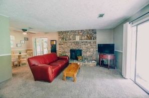 Un salón con un sofá de cuero rojo, una mesa de centro de madera, una chimenea de piedra y un televisor sobre un mueble de madera.