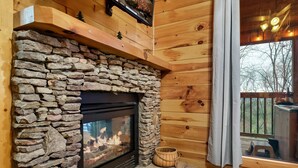 A stone fireplace with a black glass door, wooden beams, and a small wooden shelf above it. - Spacious Cozy Cabin - Best of Both Worlds (Gatlinburg)