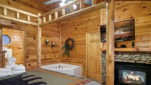 A log cabin interior with a stone fireplace, a bathtub, and a large window. - Spacious Cozy Cabin - Best of Both Worlds (Gatlinburg)